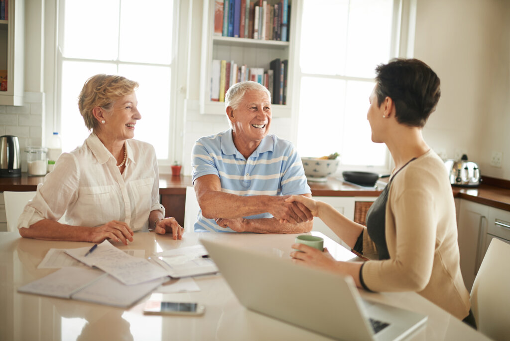 Three people sitting at a kitchen table with a laptop.